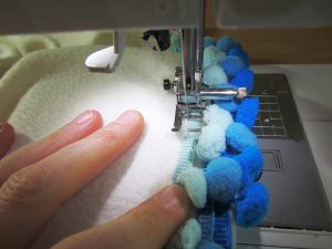 Fleece doesn’t fray when cut. Because of this, you can decide to add reinforced stitching on the longer (non-pom pom) side or not.